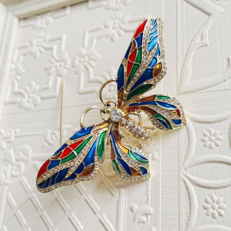 Primo piano della spilla a forma di farfalla che evidenzia il lavoro intricato di strass e smalto.