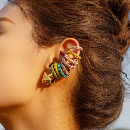 Een oor van een model versierd met een verscheidenheid aan kleurrijke rhinestone oorclips, die laat zien hoe je de set kunt stylen.