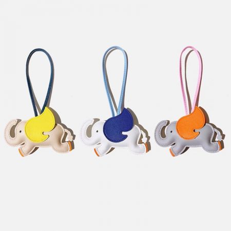 Una colección de tres coloridos charms de bolso en cuero PU de elefante en blanco, gris y marfil, mostrando las opciones de color disponibles.