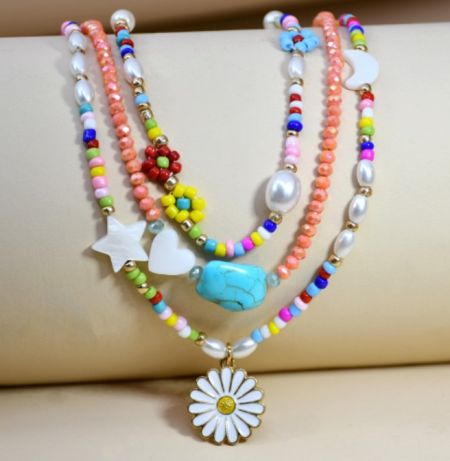 Five distinct beaded necklaces layered together, featuring different charms and pendants.