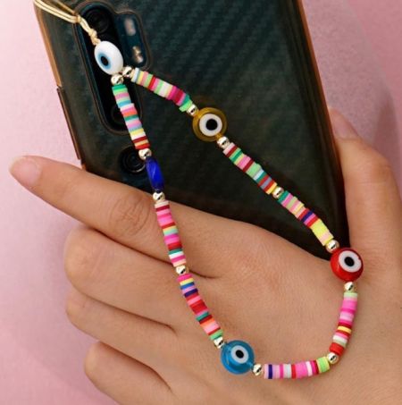 Close-up de um charm de telefone colorido com contas em forma de olho preso a uma capa de smartphone.