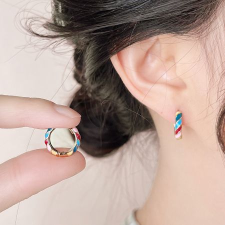 Une paire de créoles huggie en or avec un design en émail rouge, blanc et bleu.