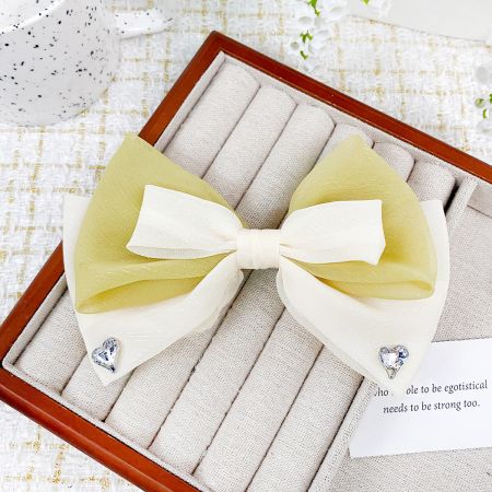 Close-up of a ribbon bow hair clip featuring a delicate heart-shaped gem embellishment.