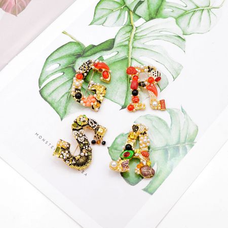 Una disposición artística de broches de letras barrocas sobre hojas de monstera, mostrando su atractivo versátil y decorativo.