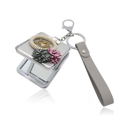 The compact mirror shown with various decorative elements including a beaded bracelet and pinecone charms, highlighting its versatility as a fashion accessory.