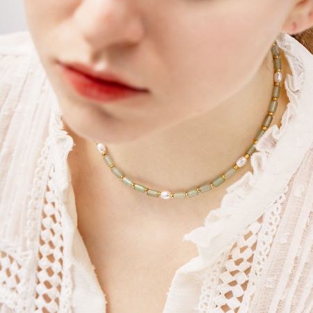 Primer plano de un delicado collar con cuentas gris verdosas, perlas blancas y sutiles acentos dorados.