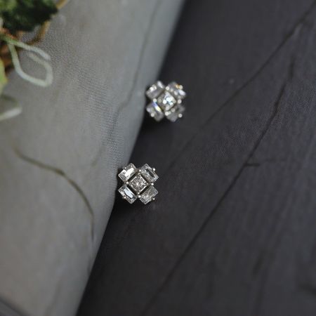Orecchini a perno in zirconia cubica a forma di cubo di ghiaccio in argento sterling 925 (5 paia) - Un paio di orecchini a perno in argento sterling 925 a forma di cubo di ghiaccio con zirconia cubica, esposti su una superficie in legno scuro.