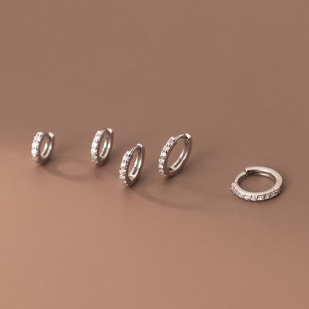Una collezione di cinque orecchini a cerchio huggie in argento sterling 925 con zirconia in varie dimensioni.