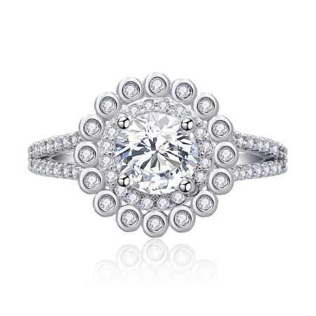 Rond geslepen gesplitste shank verlovingsring - Een close-up van de rond geslepen gesplitste shank verlovingsring, met een briljante cubic zirconia centrale steen in een halo-instelling op een rhodium-geplateerde band.