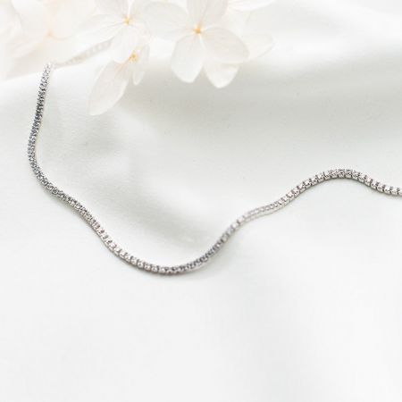 Gros plan sur le collier en zircon de tennis en argent sterling 925 sur un fond blanc avec des fleurs délicates.