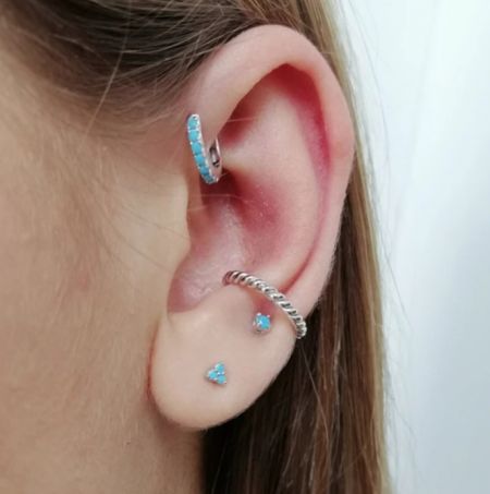La oreja del modelo adornada con los elegantes aretes huggie y de perno en oro y turquesa.