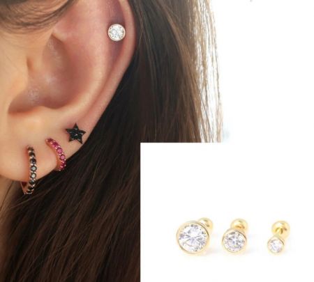 Un orecchio di un modello adornato con vari orecchini a perno in zirconia cubica dorata, che dimostra diverse posizioni di piercing.