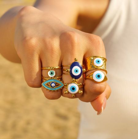 Groothandel roestvrijstalen boze oogringen - De hand van een model die een collectie elegante vergulde roestvrijstalen boze oogringen van JR Fashion Accessories toont.