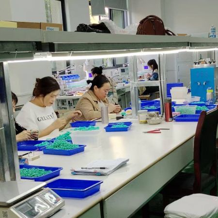Trabajadores en la línea de ensamblaje de la fábrica en JR Fashion Accessories, demostrando el proceso de producción de joyería ecológica.