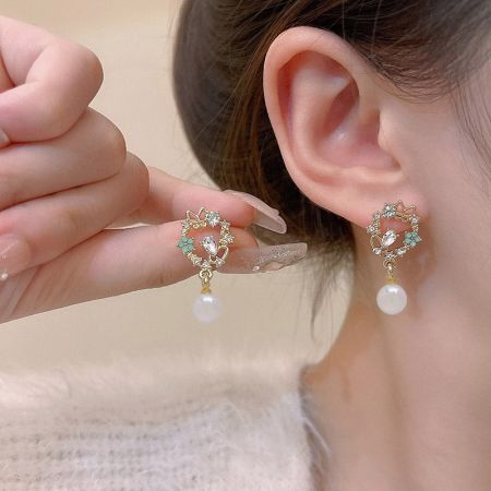 金のクリップオンイヤリングの花柄デザインのクローズアップで、透明でライトブルーの宝石と白い真珠が見えます。