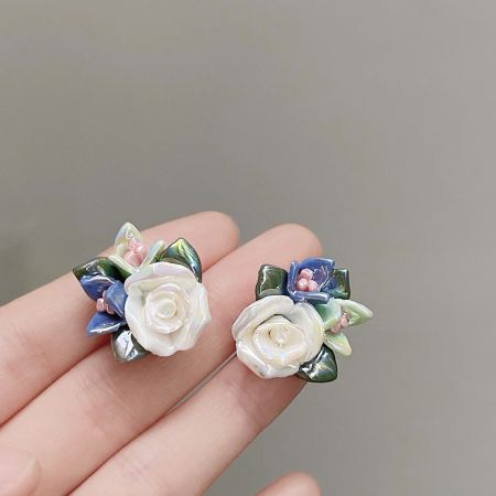 繊細な青い花のアクセントが施された白い陶器の花のイヤリングのペア。