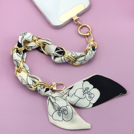 黒と白の花柄シルクスカーフの携帯ストラップ、金のアクセント付きのクローズアップ。