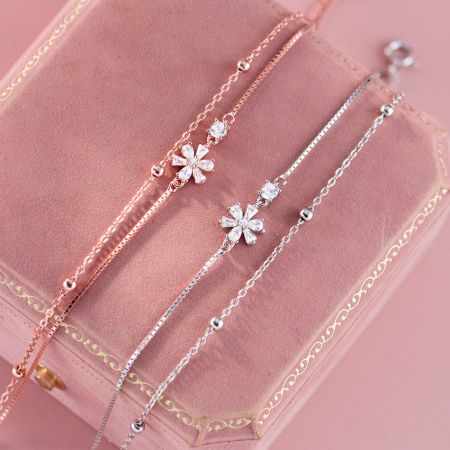 Dames 925 sterling zilveren bloemen zirconia delicate dubbele laag armband - Een set van drie elegante 925 sterling zilveren armbanden met sprankelende cubic zirconia bloemencharms, tentoongesteld in een roze juwelendoos.