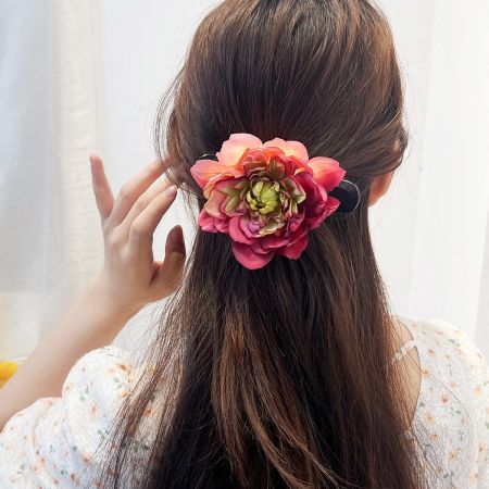 A model with long brown hair wearing a large pink peony flower claw hairclip.