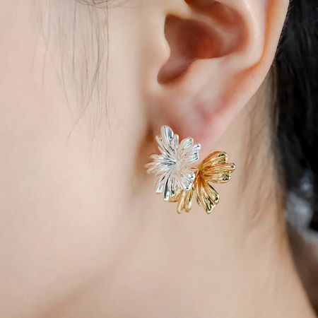 シルバーとゴールドのトーンで、両面着用可能な花のスタッドイヤリングを紹介するモデル。