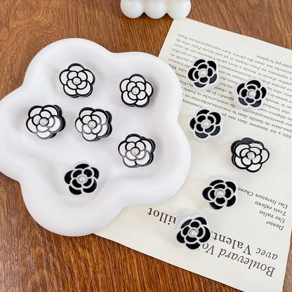 Een assortiment van zwarte en witte camelia bloem haarclips samen weergegeven.