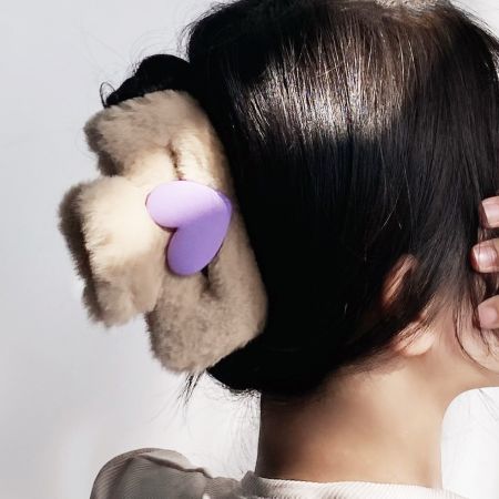 Primer plano de un clip de pelo beige esponjoso con un vibrante detalle de corazón púrpura.