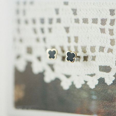 Pendientes de mariposa de esmalte negro elegantes con borde dorado, exhibidos sobre una superficie blanca decorativa.