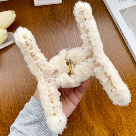 サイズと質感を示すために、大きくて快適なカーキ色のふわふわのヘアクリップを持つ手。