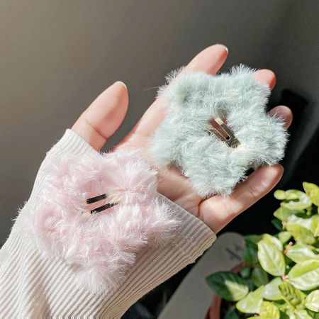 Gros plan sur les pinces à cheveux en peluche étoile rose et bleu-vert tenues dans la main, montrant la texture douce.