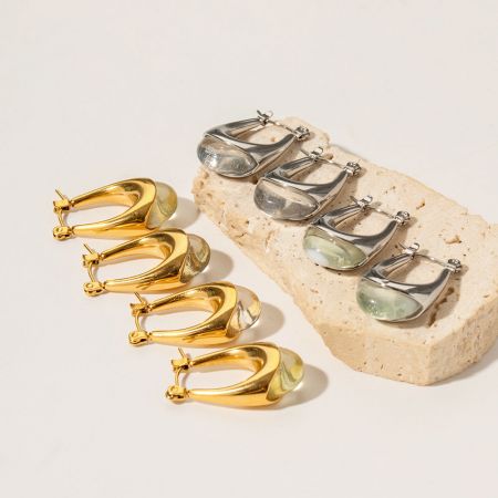 Pendientes de aro en forma de U de acero inoxidable con gema cabujón de resina clara (5 pares) - Un par de pendientes de aro en forma de U dorados y un par plateados de acero inoxidable, cada uno adornado con una gema cabujón de resina clara, exhibidos sobre un fondo neutro.