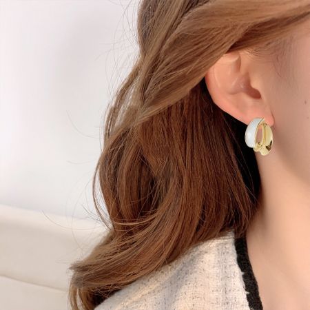 Close-up view of a geometric white enamel stud earring with 14k gold plating.