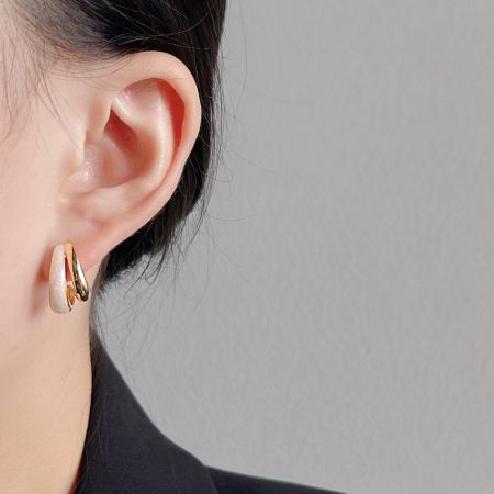 レトロセットの金と白のエナメルフープイヤリングを着用したモデル。