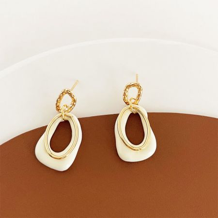 Un autre angle des élégantes boucles d'oreilles ovales dorées et blanches, montrant leur savoir-faire raffiné.