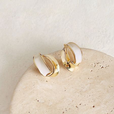 A pair of gold and white enamel earrings from the set, artfully placed on a beige decorative stone.