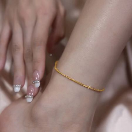 Sprankelende 925 zilveren delicate enkelband voor vrouwen - Close-up van de enkel van een vrouw die een sprankelende goudkleurige 925 zilveren delicate enkelband draagt, perfect voor speciale gelegenheden zoals bruiloften of feesten.