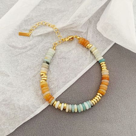 Primer plano de una pulsera boho apilable con cuentas de piedra natural en naranja, blanco y dorado.