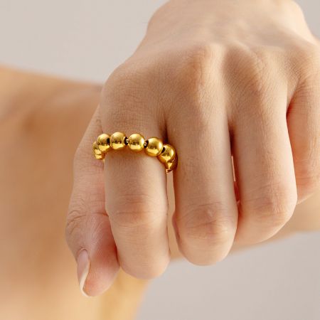 Ringen met een open verstelbaar ontwerp van roestvrij staal met punkkralen - Set van 5 - De hand van een model die de verstelbare ring van roestvrij staal met punk kralenbal in een gouden afwerking draagt, en het elegante ontwerp toont.