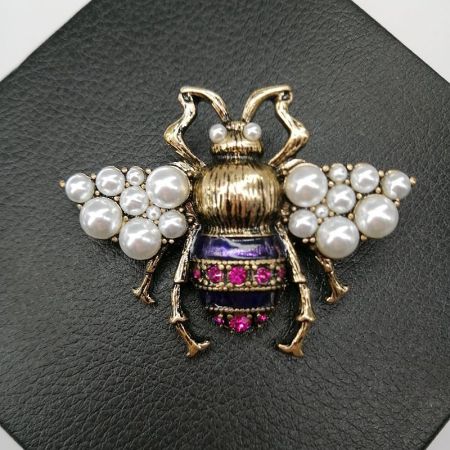 Vintage Bronze Bee Brooch with Pearl & Yellow Enamel – Galaxy Memory Collection - A detailed close-up of the Vintage Bronze Bee Brooch, highlighting its antique gold finish, faux pearl wings, and purple enamel body with magenta rhinestone accents.