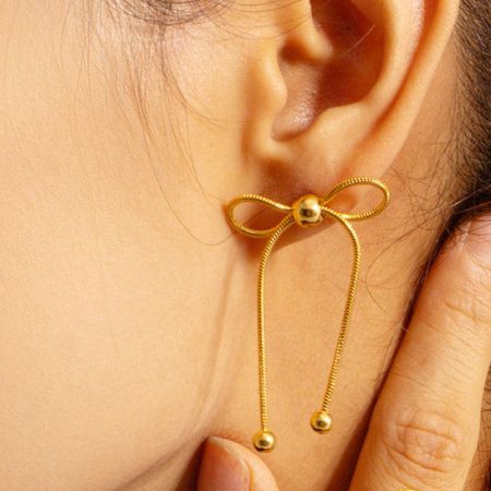 Primer plano detallado de un solo pendiente de aro con nudo dorado.