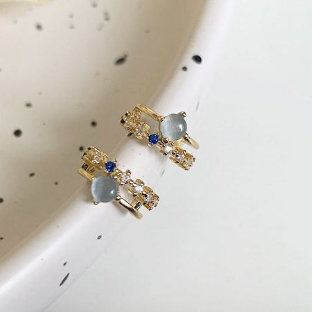 グレーと青の石で飾られたセットのエレガントな金のリボン型ピアス。