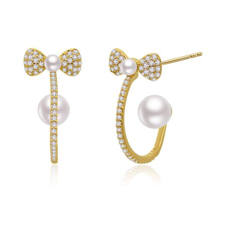 Primer plano de los elegantes pendientes de perlas con lazo de oro, destacando los detalles engastados en diamantes y la gran perla blanca.
