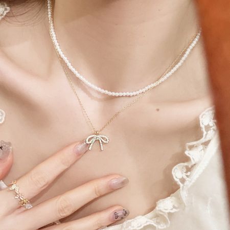 Un look élégant avec le collier en or à nœud en couches et un collier de perles classique.