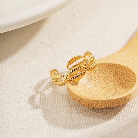 Artistieke weergave van een gouden cowrie-schelp ring op een houten lepel, die de textuur benadrukt.
