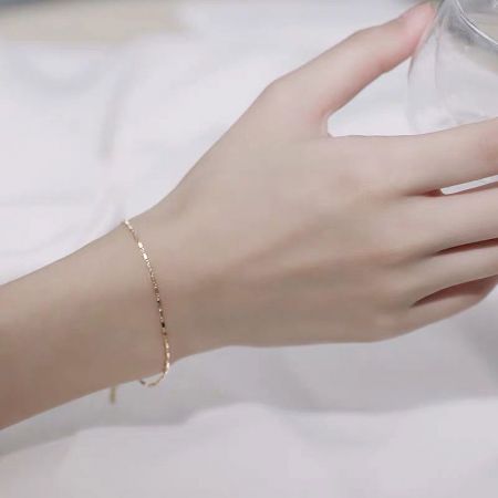 Una modelo lleva la pulsera de cadena de geometría cuadrada dorada y delgada, mostrando su ajuste elegante en la muñeca.