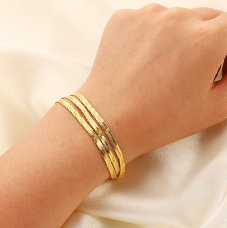 Roestvrijstalen drievoudig gelaagde platte slangenkettingarmbanden (set van 5) - Een close-up van de roestvrijstalen drievoudig gelaagde platte slangenkettingarmband in een stralende gouden afwerking, die de ingewikkelde textuur en het ontwerp toont.