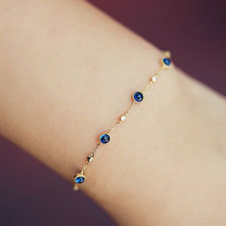 Brazaletes de cadena chapados en oro de plata esterlina 925 con circonios azules al por mayor (conjunto de 5) - Un impresionante brazalete de plata esterlina 925 chapado en oro de un conjunto al por mayor, con circonios azules brillantes y piedras de acento claras sobre un fondo blanco.