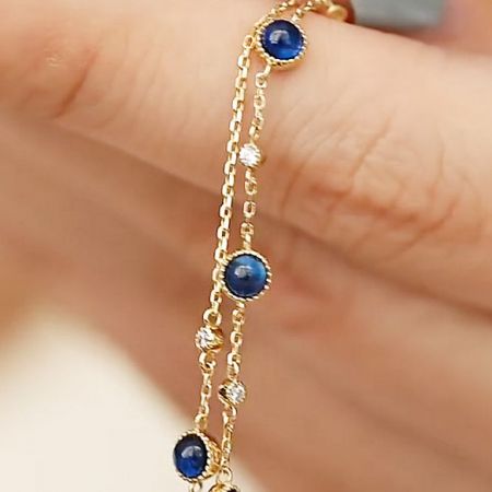 Modell trägt ein vergoldetes Armband aus Sterlingsilber mit blauen Zirkonsteinen, um die Passform zu zeigen.