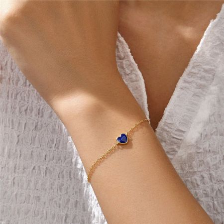 Model wearing the gold chain bracelet with a vibrant blue enamel heart charm.