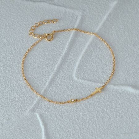 925 sterling zilveren gouden kruis armband met cubic zirconia voor vrouwen - Een delicate 925 sterling zilveren armband in goudkleur met een zijwaarts kruis charme en een sprankelende cubic zirconia steen op een witte achtergrond.