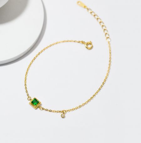 925 Sterling Zilveren Smaragd Vergulde Armband - Een close-up van de 925 Sterling Zilveren Smaragd Vergulde Armband, met de groene smaragd en heldere cubic zirconia edelstenen op een gouden ketting.